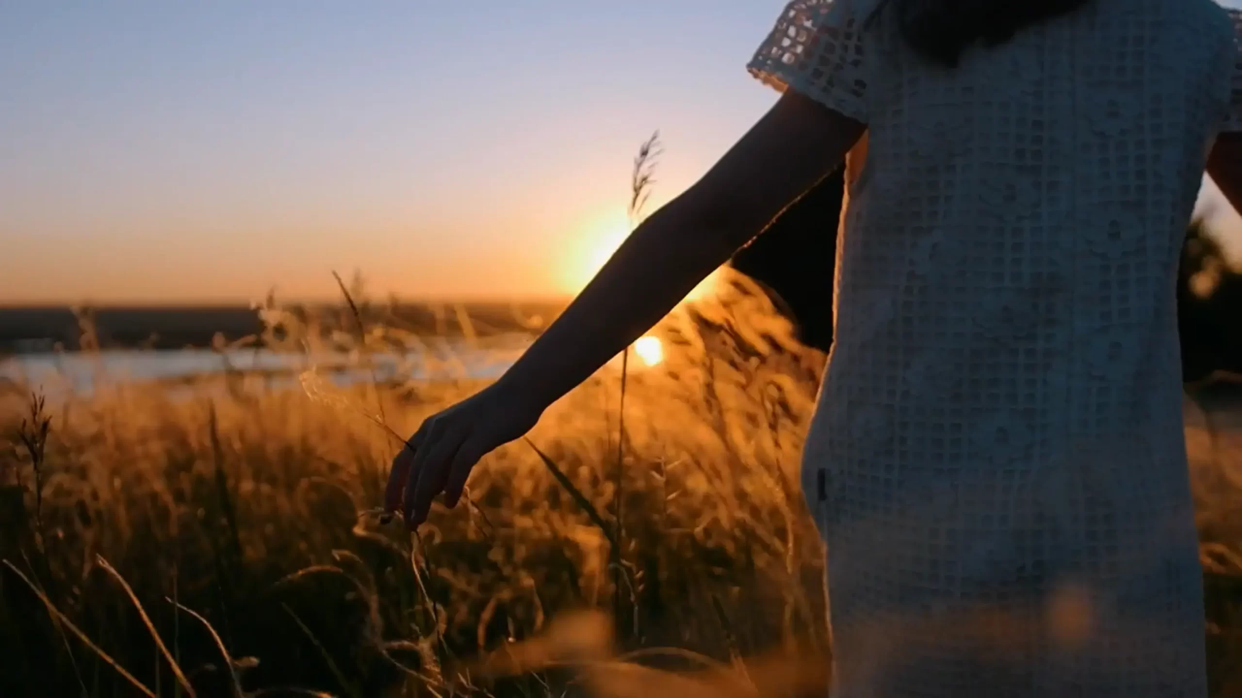 Girl in a dress caressing the grass at sunset